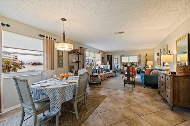 dining area with a textured ceiling, light tile patterned floors, and a water view