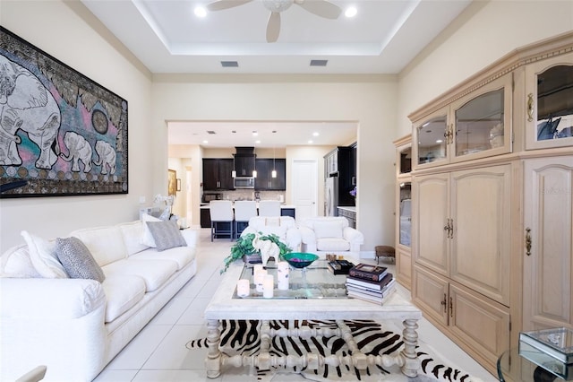 living room featuring a raised ceiling, ceiling fan, and light tile patterned flooring