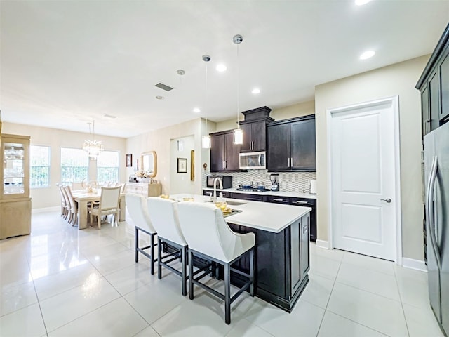 kitchen featuring dark brown cabinetry, hanging light fixtures, stainless steel appliances, an island with sink, and a kitchen bar