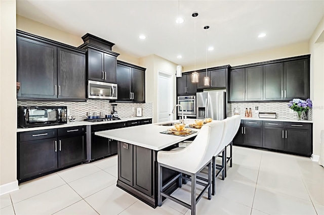 kitchen featuring decorative backsplash, hanging light fixtures, appliances with stainless steel finishes, and an island with sink