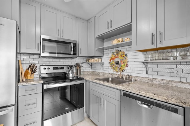 kitchen with decorative backsplash, light stone counters, sink, and appliances with stainless steel finishes