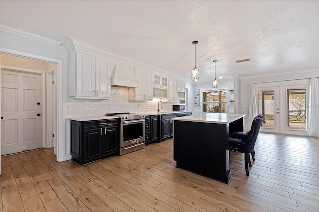 kitchen featuring a breakfast bar, premium range hood, white cabinets, decorative backsplash, and stainless steel range with electric cooktop