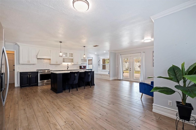 kitchen featuring electric stove, crown molding, premium range hood, white cabinetry, and an island with sink