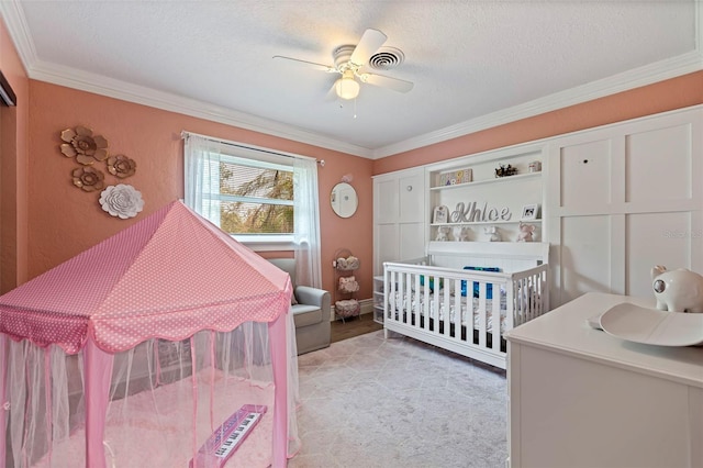 bedroom featuring a nursery area, ceiling fan, crown molding, and a textured ceiling