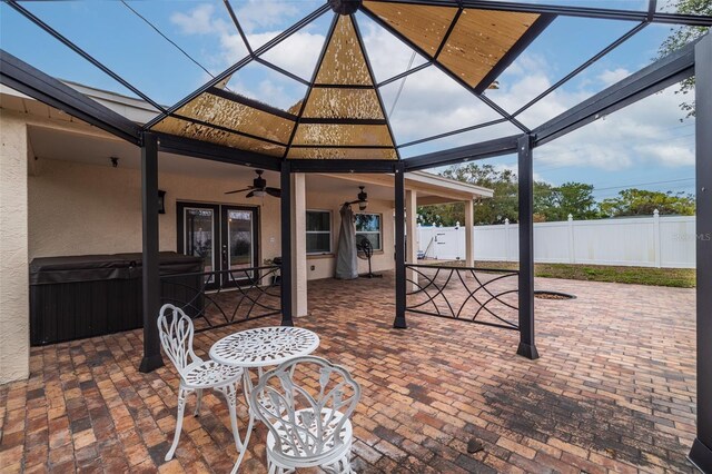 view of patio featuring a hot tub, ceiling fan, and glass enclosure