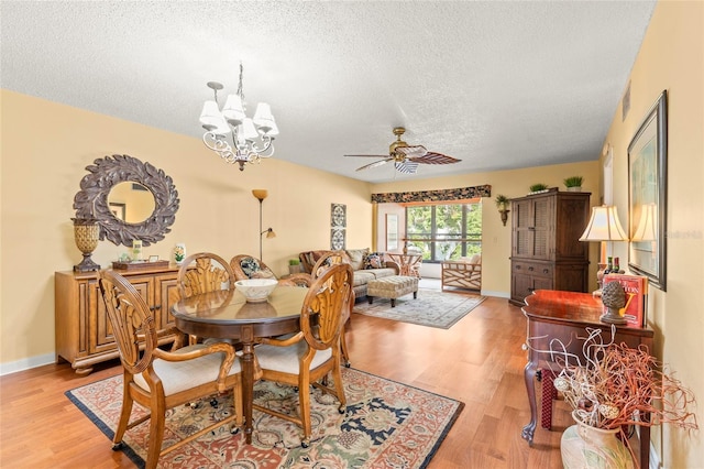 dining space featuring ceiling fan with notable chandelier, a textured ceiling, and light hardwood / wood-style flooring