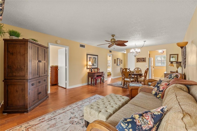 living room with hardwood / wood-style flooring, ceiling fan with notable chandelier, and a textured ceiling