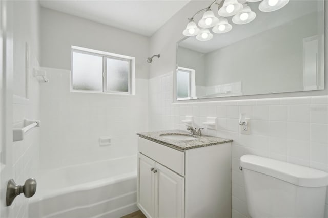 full bathroom with vanity, toilet, tiled shower / bath, and tile walls