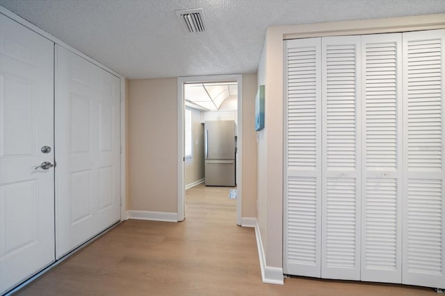 corridor with light wood-type flooring and a textured ceiling