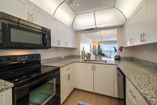 kitchen with black appliances, sink, white cabinets, light stone counters, and light hardwood / wood-style floors