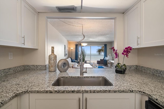 kitchen with white cabinetry, light stone countertops, sink, and a textured ceiling