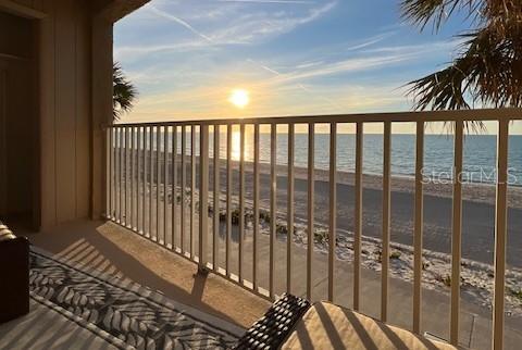 balcony at dusk with a water view and a view of the beach