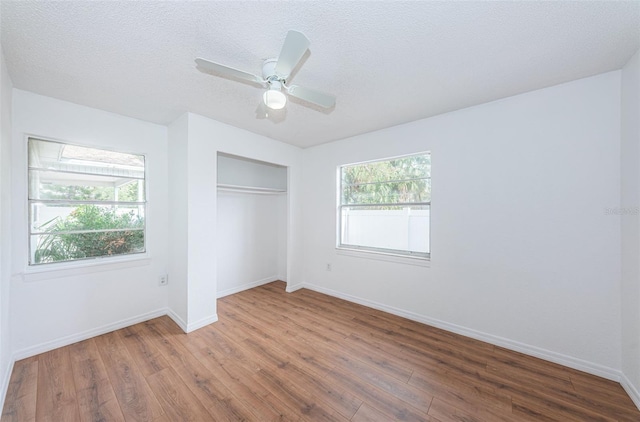 unfurnished bedroom featuring hardwood / wood-style floors, ceiling fan, multiple windows, and a closet