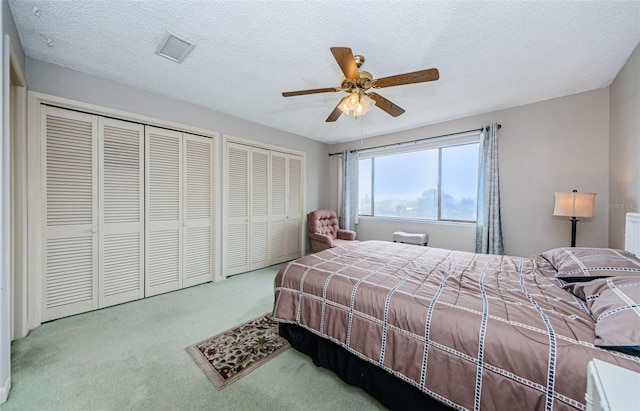 carpeted bedroom featuring a textured ceiling, ceiling fan, and multiple closets