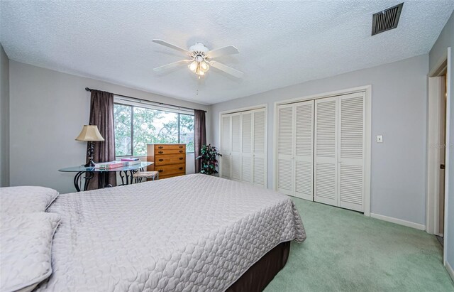 carpeted bedroom with a textured ceiling, ceiling fan, and multiple closets