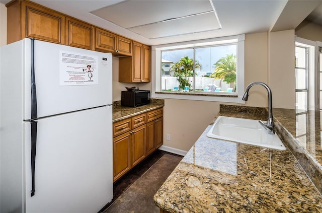 kitchen featuring stone countertops, white fridge, and sink