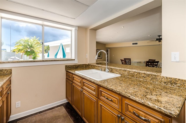 kitchen with ceiling fan, light stone countertops, kitchen peninsula, and sink