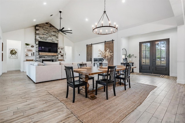 dining room featuring ceiling fan with notable chandelier, a barn door, a fireplace, and high vaulted ceiling