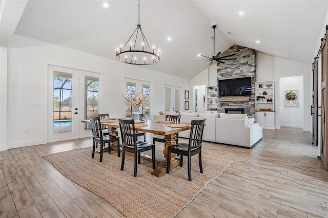 dining room with a stone fireplace, high vaulted ceiling, and ceiling fan with notable chandelier