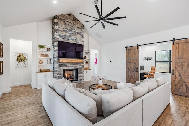 living room with a stone fireplace, vaulted ceiling, light hardwood / wood-style flooring, ceiling fan, and a barn door