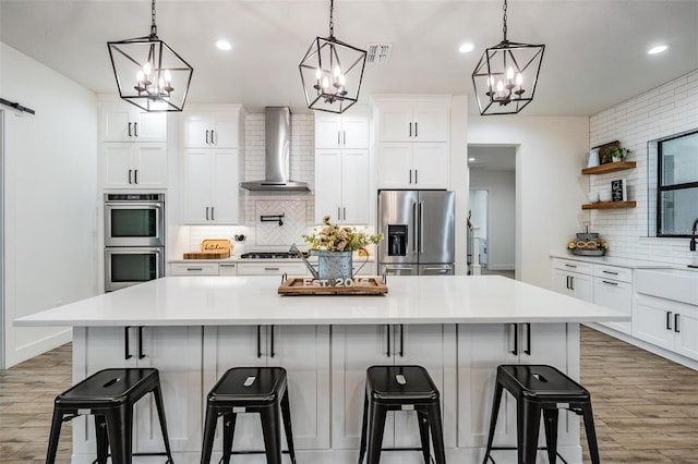 kitchen featuring stainless steel appliances, wall chimney range hood, backsplash, a spacious island, and a kitchen bar