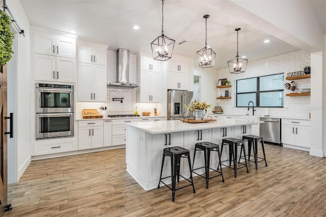 kitchen with white cabinetry, a center island, stainless steel appliances, and wall chimney range hood