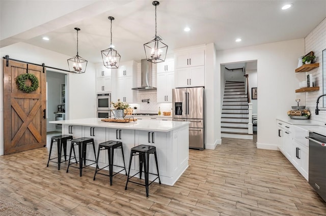 kitchen with a kitchen breakfast bar, wall chimney exhaust hood, a barn door, white cabinetry, and stainless steel appliances