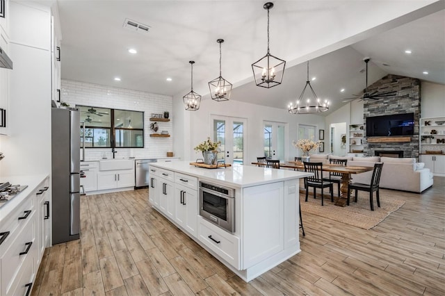 kitchen featuring a center island, hanging light fixtures, a fireplace, appliances with stainless steel finishes, and white cabinetry