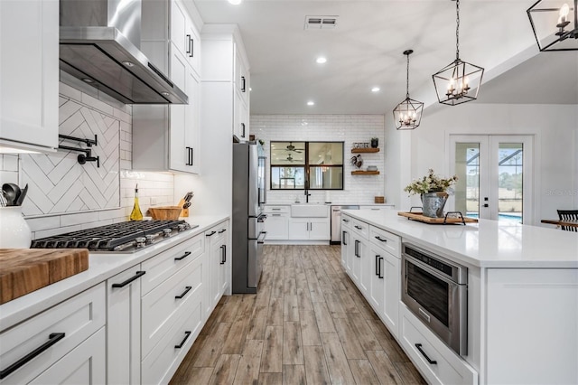 kitchen with white cabinets, wall chimney range hood, appliances with stainless steel finishes, and french doors