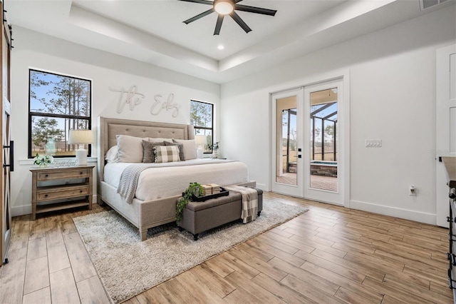 bedroom featuring multiple windows, access to outside, french doors, ceiling fan, and a tray ceiling