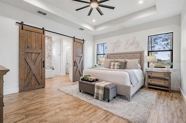 bedroom with a raised ceiling, a barn door, ceiling fan, and ensuite bathroom