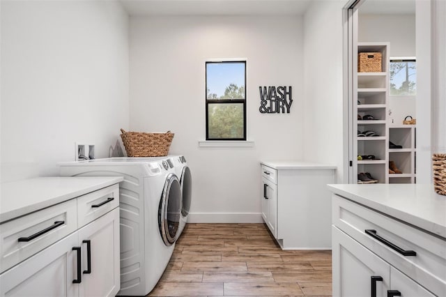 clothes washing area with cabinets, light wood-type flooring, and washing machine and dryer