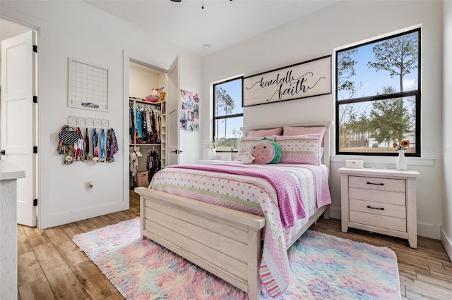 bedroom featuring light hardwood / wood-style flooring, a spacious closet, multiple windows, and a closet