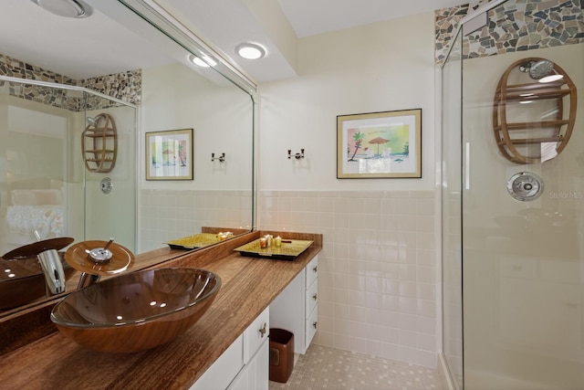 bathroom with a shower with shower door, tile walls, vanity, and tile patterned flooring