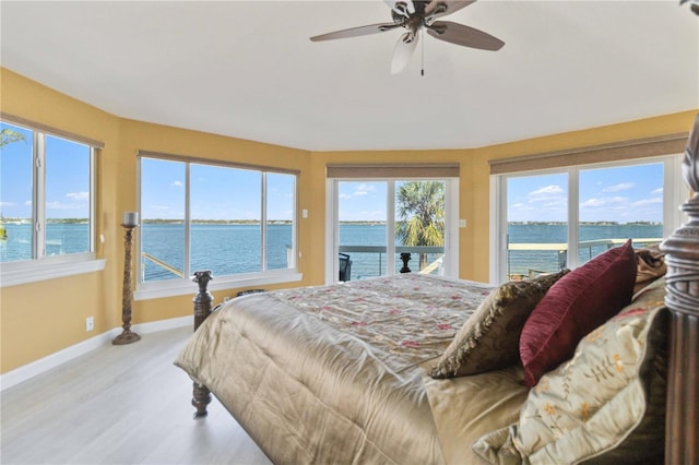 bedroom featuring ceiling fan, light hardwood / wood-style floors, access to outside, and a water view