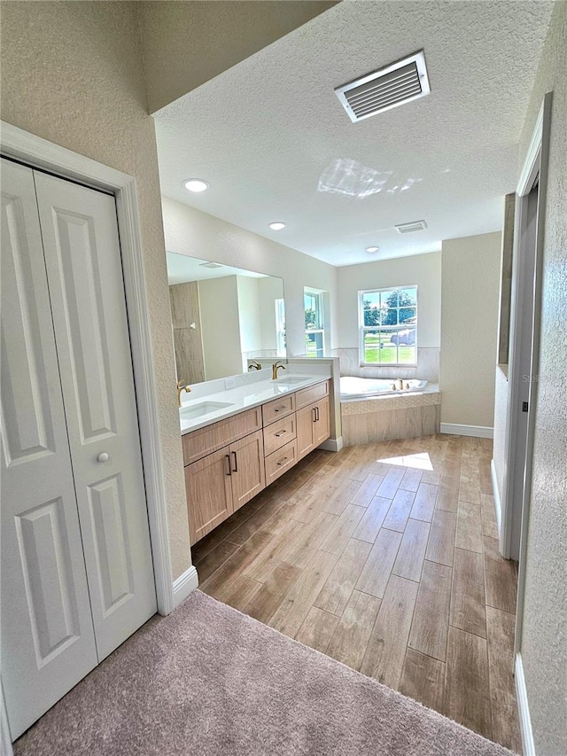 bathroom featuring tiled tub, vanity, and a textured ceiling