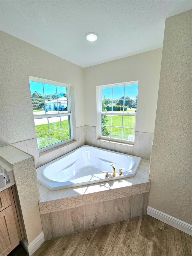 bathroom featuring wood-type flooring, vanity, tiled bath, and a textured ceiling