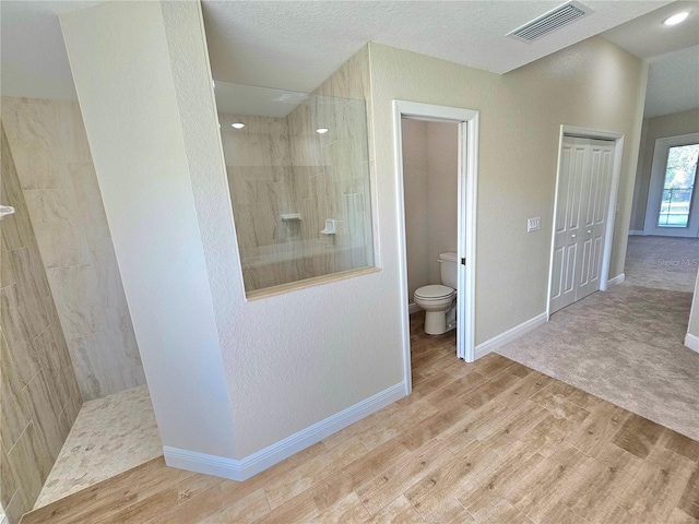 bathroom with toilet, wood-type flooring, and tiled shower