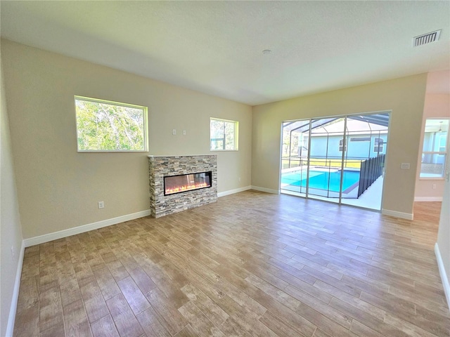 unfurnished living room with a stone fireplace, plenty of natural light, and light hardwood / wood-style flooring