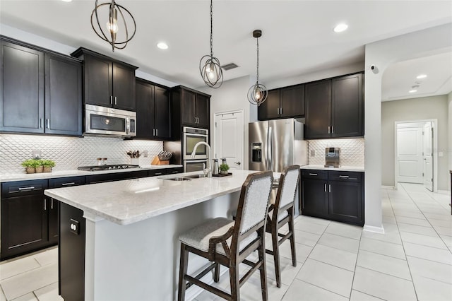 kitchen featuring light stone countertops, backsplash, stainless steel appliances, and an island with sink