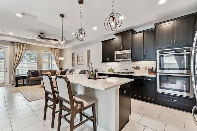 kitchen with appliances with stainless steel finishes, ceiling fan, sink, a center island with sink, and hanging light fixtures