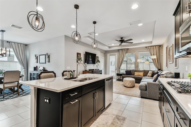 kitchen with sink, stainless steel appliances, an island with sink, decorative light fixtures, and a tray ceiling