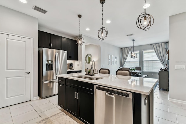 kitchen featuring a center island with sink, sink, decorative light fixtures, light tile patterned flooring, and stainless steel appliances