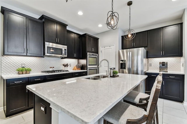 kitchen featuring appliances with stainless steel finishes, backsplash, light tile patterned floors, decorative light fixtures, and an island with sink