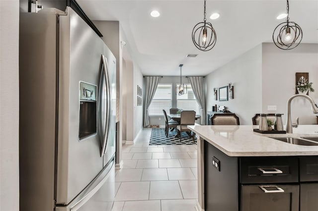 kitchen featuring pendant lighting, sink, stainless steel fridge, light tile patterned floors, and light stone counters