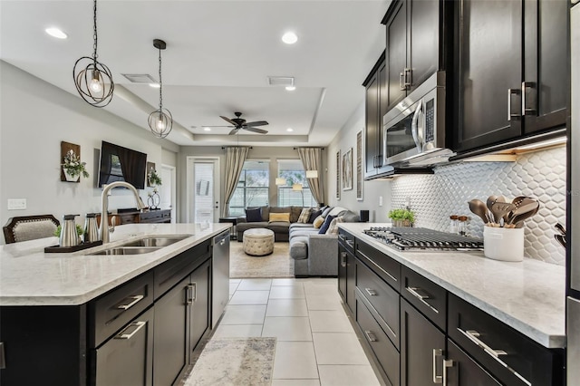 kitchen with appliances with stainless steel finishes, tasteful backsplash, a raised ceiling, a kitchen island with sink, and sink