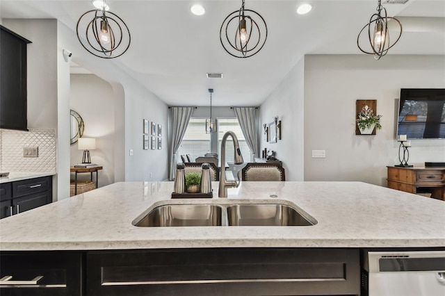 kitchen featuring dishwasher, sink, hanging light fixtures, and an island with sink