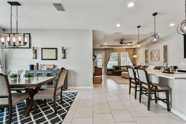 tiled dining space with ceiling fan with notable chandelier and a tray ceiling