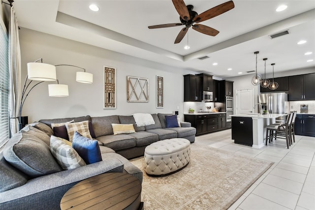 living room featuring a raised ceiling, ceiling fan, sink, and light tile patterned flooring