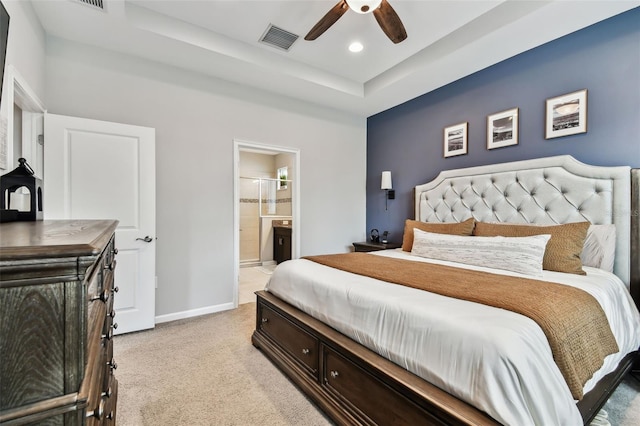 bedroom with light carpet, connected bathroom, a raised ceiling, and ceiling fan